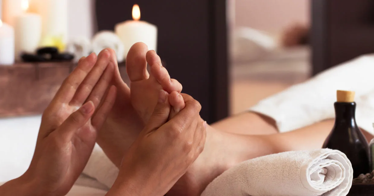 Foot spa massage — therapist's hands cradling a foot, candles, white towels